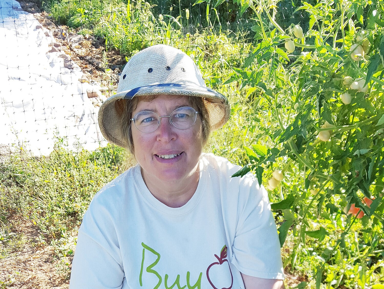 A woman in a garden wearing a hate and glasses.