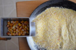 Whole corn kernels in a grinder over a bowl of ground up corn