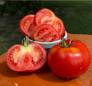 Tomatoes sliced in a bowl, halved, and whole on a table.