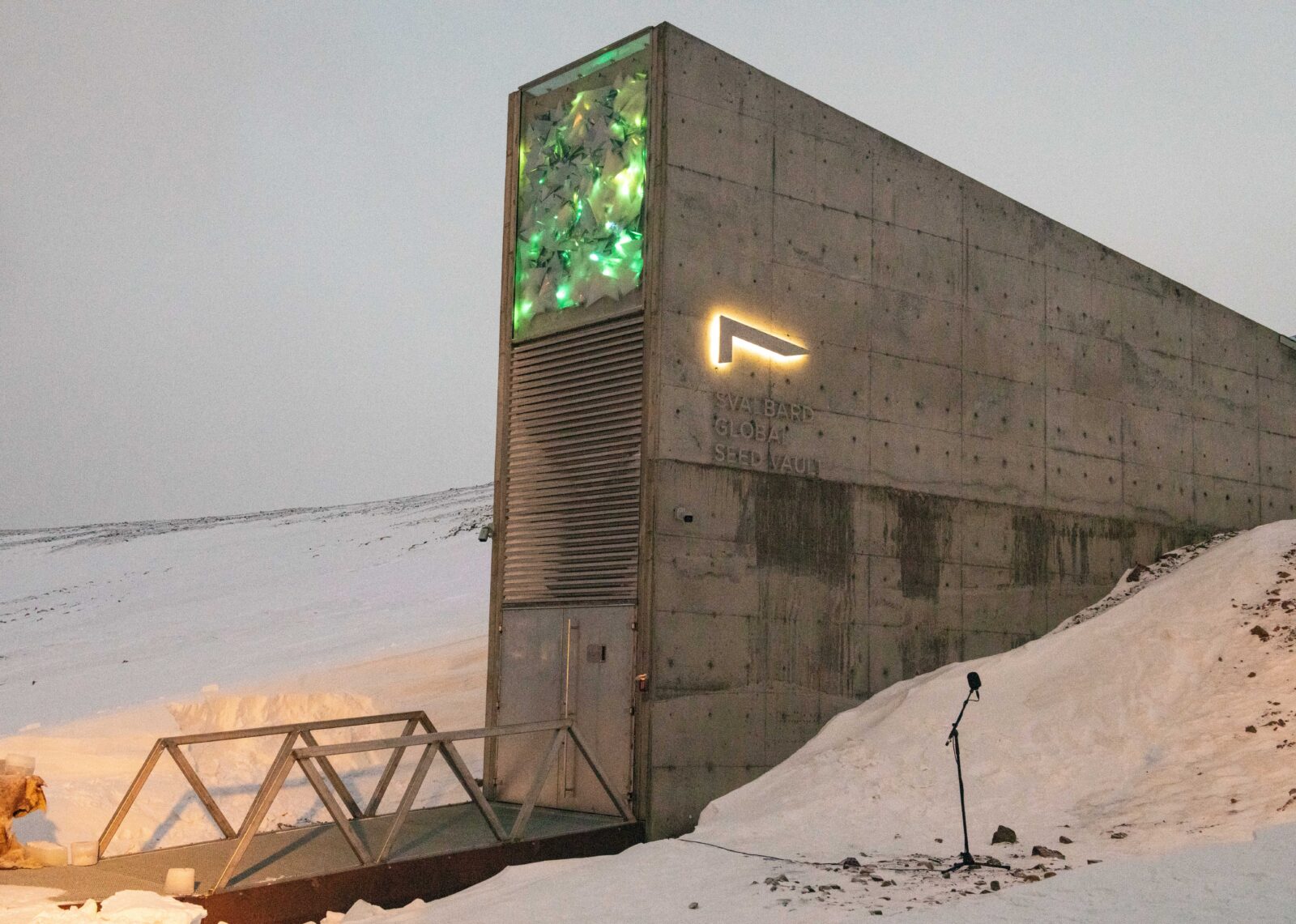 long, narrow gray building with emerald-green, glass-like art on top of front of building; building is emerging from snow bank and has bridge leading to it