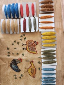 yarn samples in many different colors alongside embroidered images of three chickens