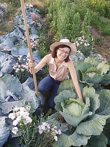 A woman poses in a garden next to rows of cabbage plants