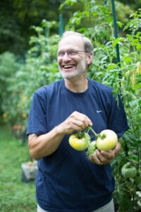 A man smiles and holds several large green tomatoes