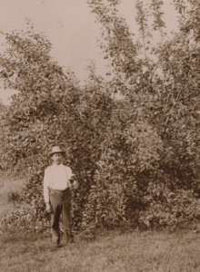 black-and_white photo of man in a hat standing in an apple orchard