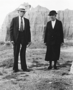 black-and_white photo of an older man wearing suit and tie and older woman wearing a long skirt and jacket