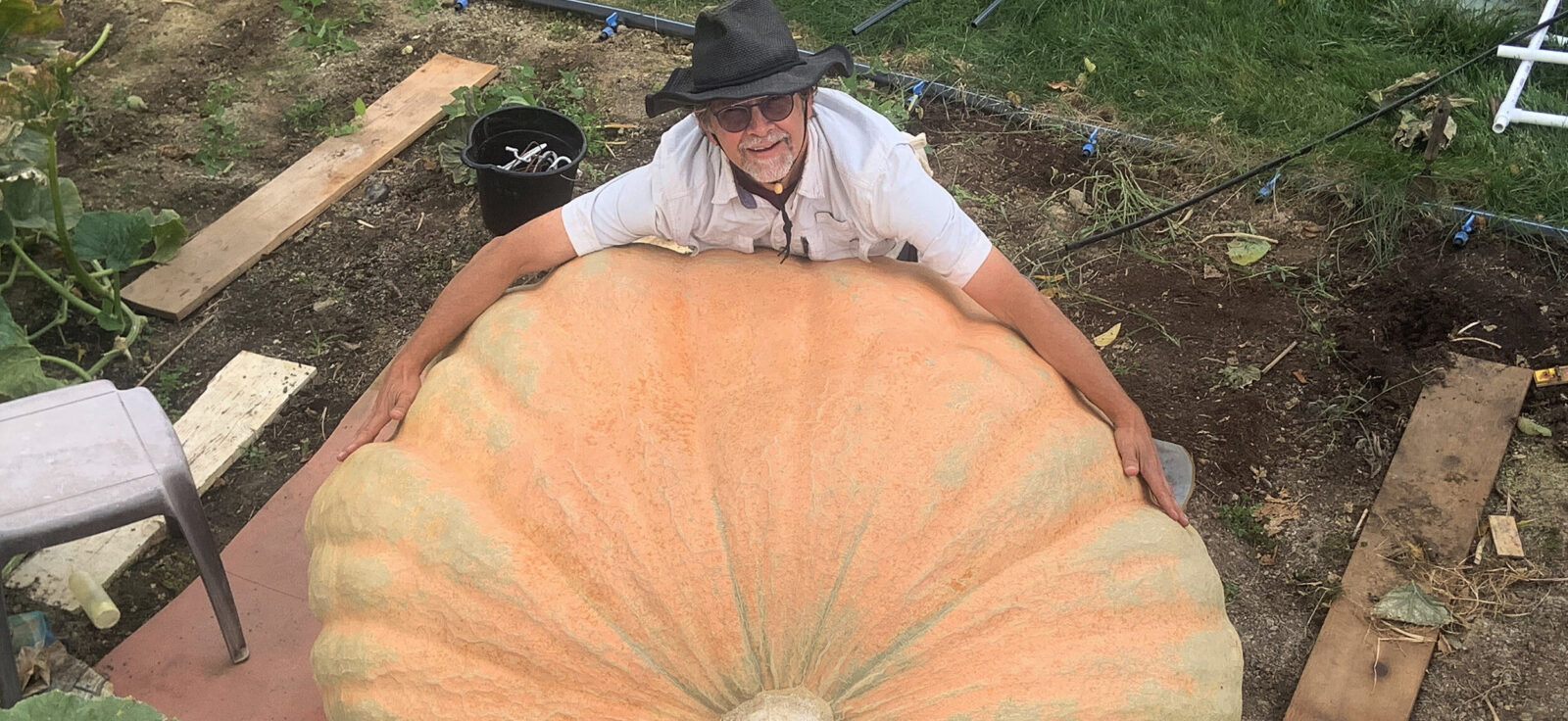 A man wraps his arms around a giant pumpkin resting on the ground