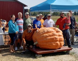 A crowd of people pose around a giant pumpkin