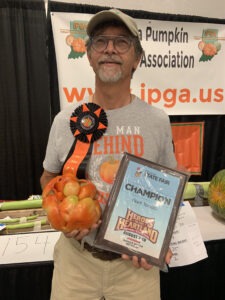 A man poses wearing a ribbon and holding a giant tomato and a "champion" plaque