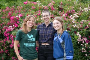 three smiling women pose in front of a backdrop of garden flowers