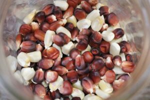 A small glass jar with colorful red and pale yellow corn seeds