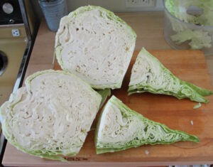 A conical cabbage sliced length-wise in half, then sliced in half horizontally, rests on a wood cutting board