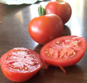 Two small red tomatoes and one halved tomato sitting on a wood table