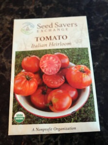 A packet of seeds with a picture of a bowl of red tomatoes that says "TOMATO Italian Heirloom"