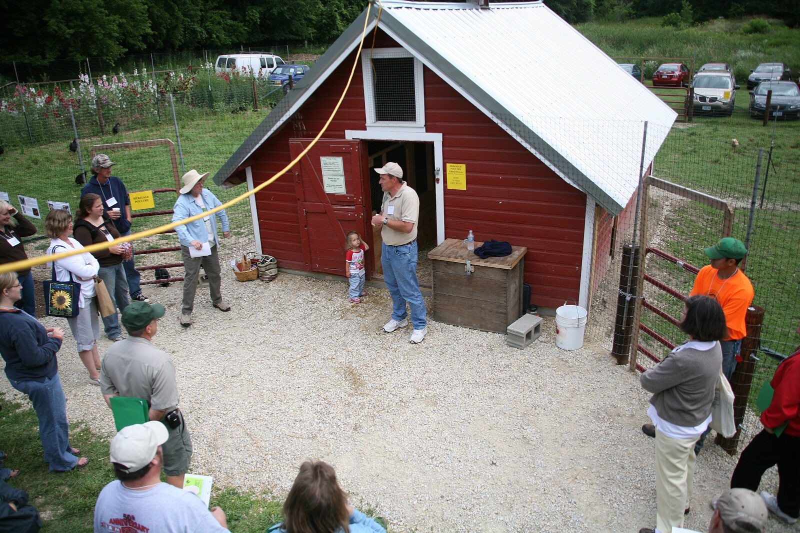 people form circle in front of small, red hen house