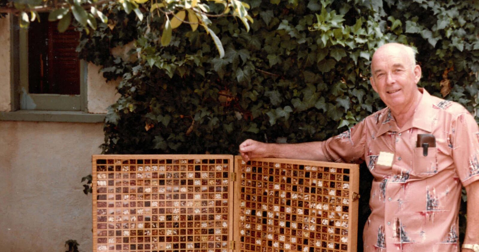John Withee Bean Display (2) An older man poses next to a large wooden case displaying hundreds of different bean varieties
