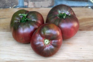 Three deep red-purple 'Cherokee Purple' tomatoes arranged on a wood cutting board.