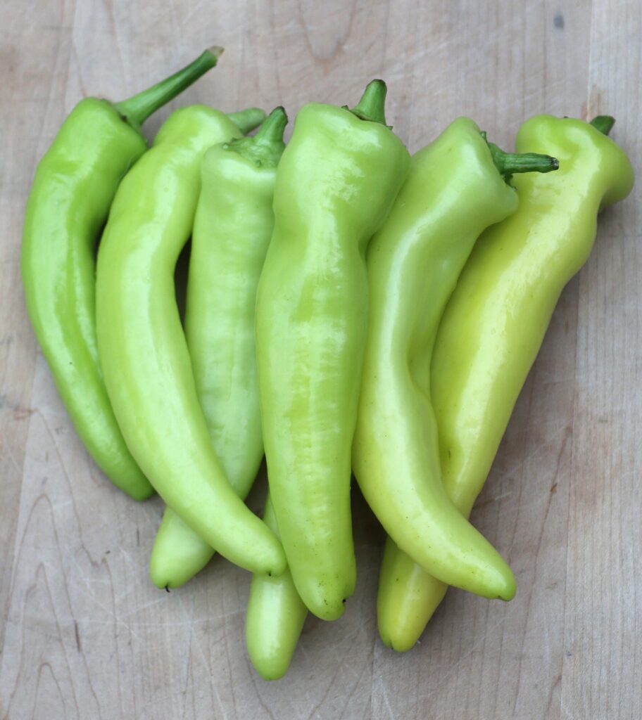 Six bright lime-green 'Hungarian Wax Hot' peppers in a line on a stone surface
