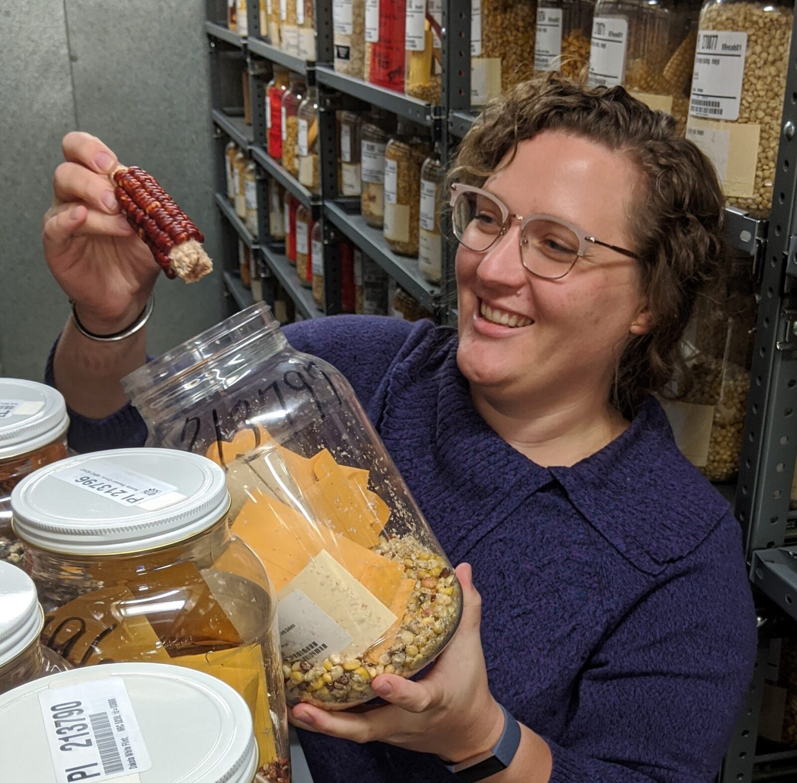 A woman smiling, holds an ear of corn and a plastic tub.